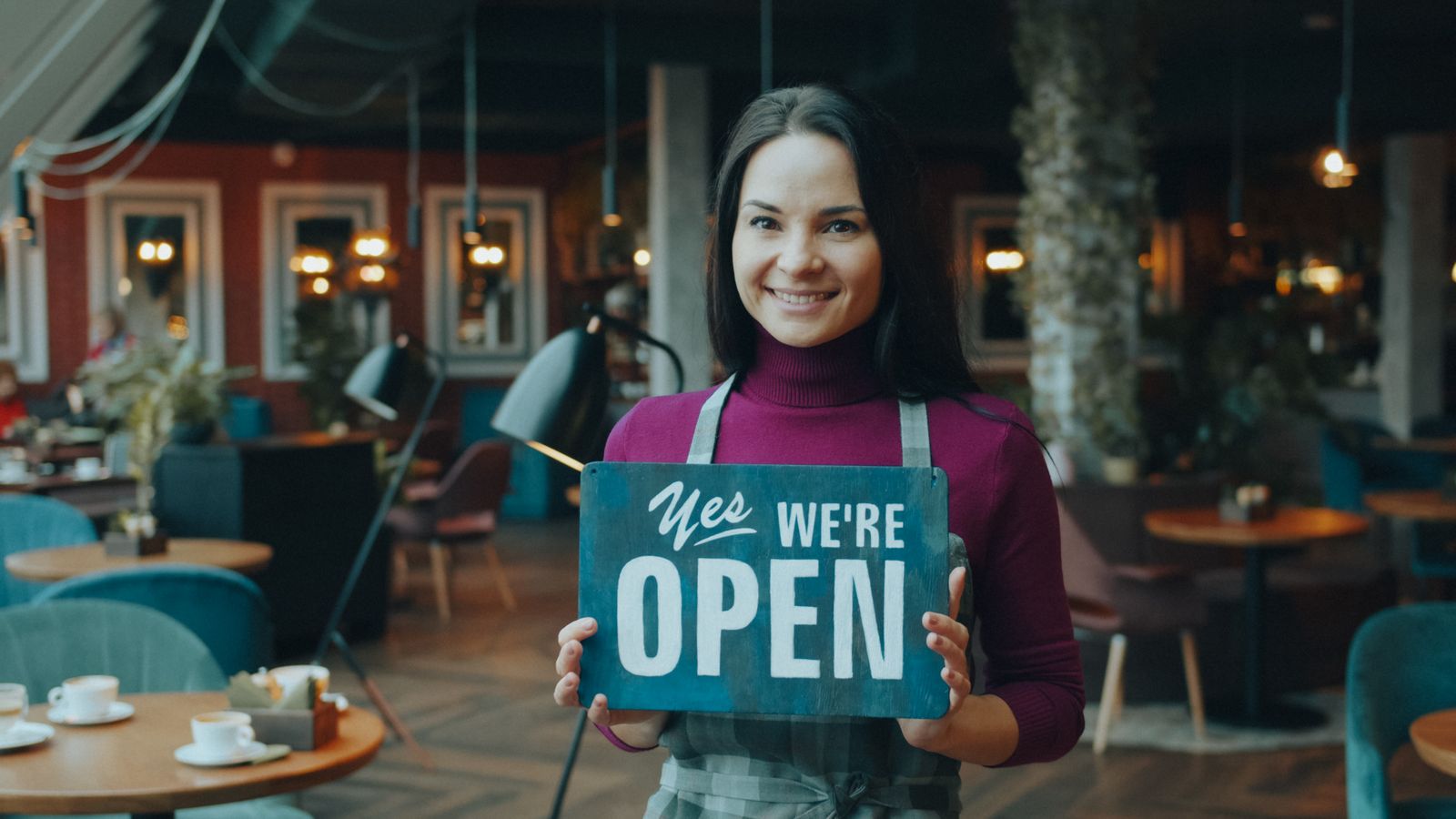 Dona de café segurando a placa de aberto